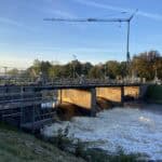 Kraan en brug boven stromend water bij zonsopgang.