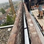 Bouwvakkers werken aan gebouwmuur met hijskraan zichtbaar.