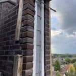 Bakstenen muur met metalen versterking en uitzicht op daken.