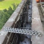 Half afgebouwde bakstenen muur met metaaldraadversterking.