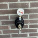 Manometer op rode bakstenen muur, drukmeter zichtbaar.